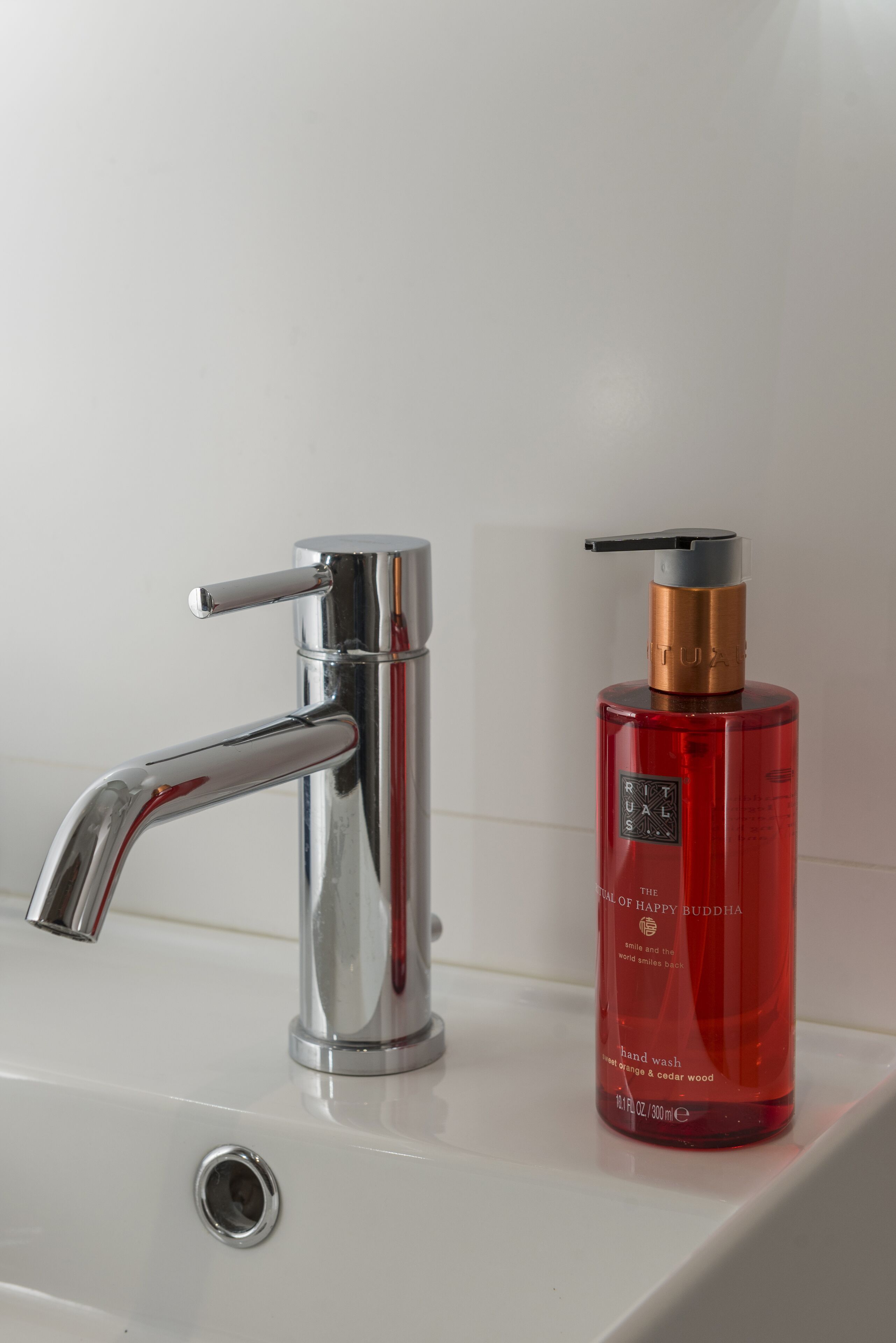 A modern bathroom sink with a chrome faucet and a red hand soap dispenser.