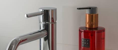 A modern bathroom sink with a chrome faucet and a red hand soap dispenser.