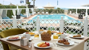 Una mesa de comedor con alimentos para el desayuno, una piscina y vistas a la playa.