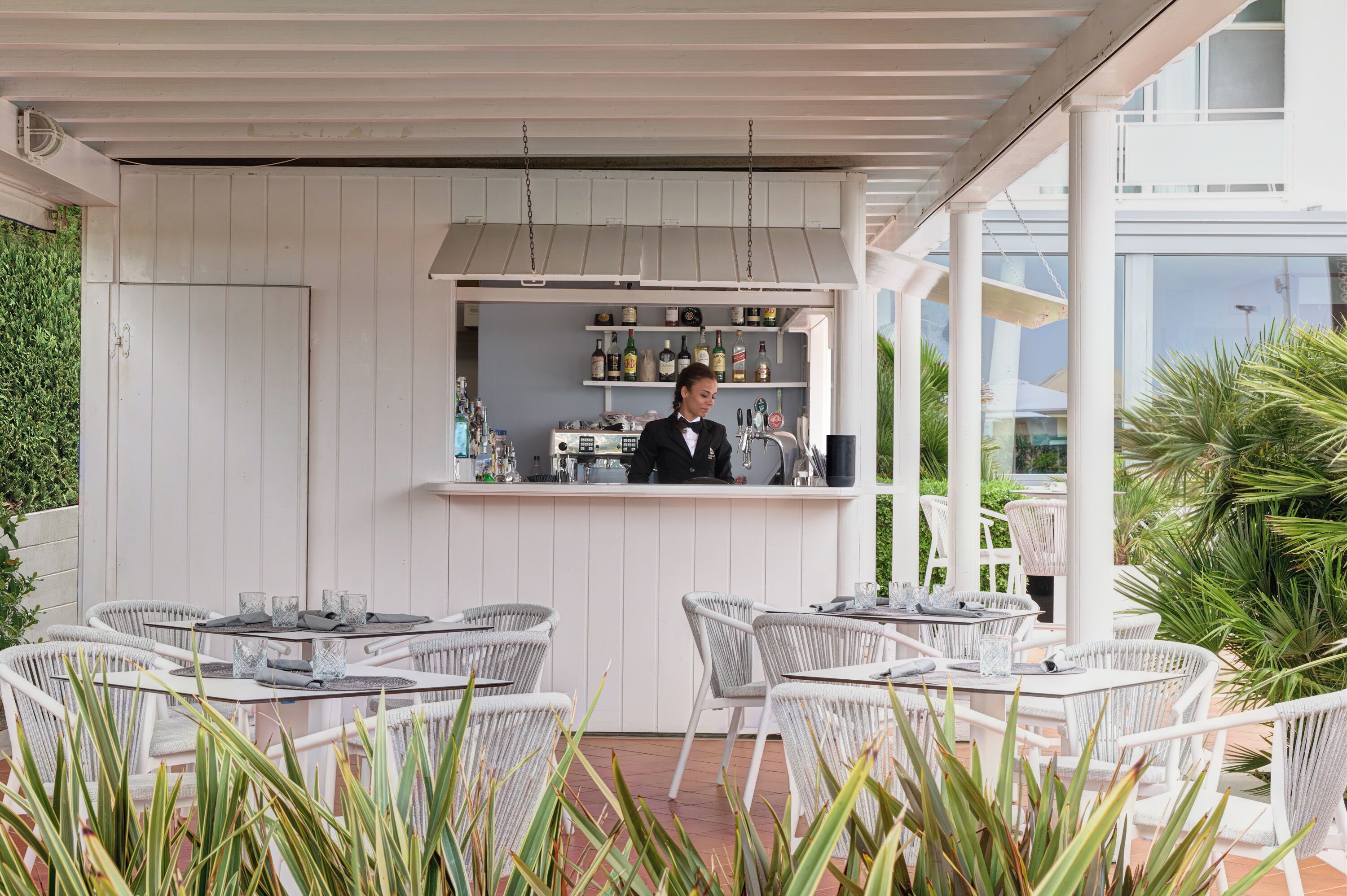 An outdoor bar area with white wicker furniture and a bartender.