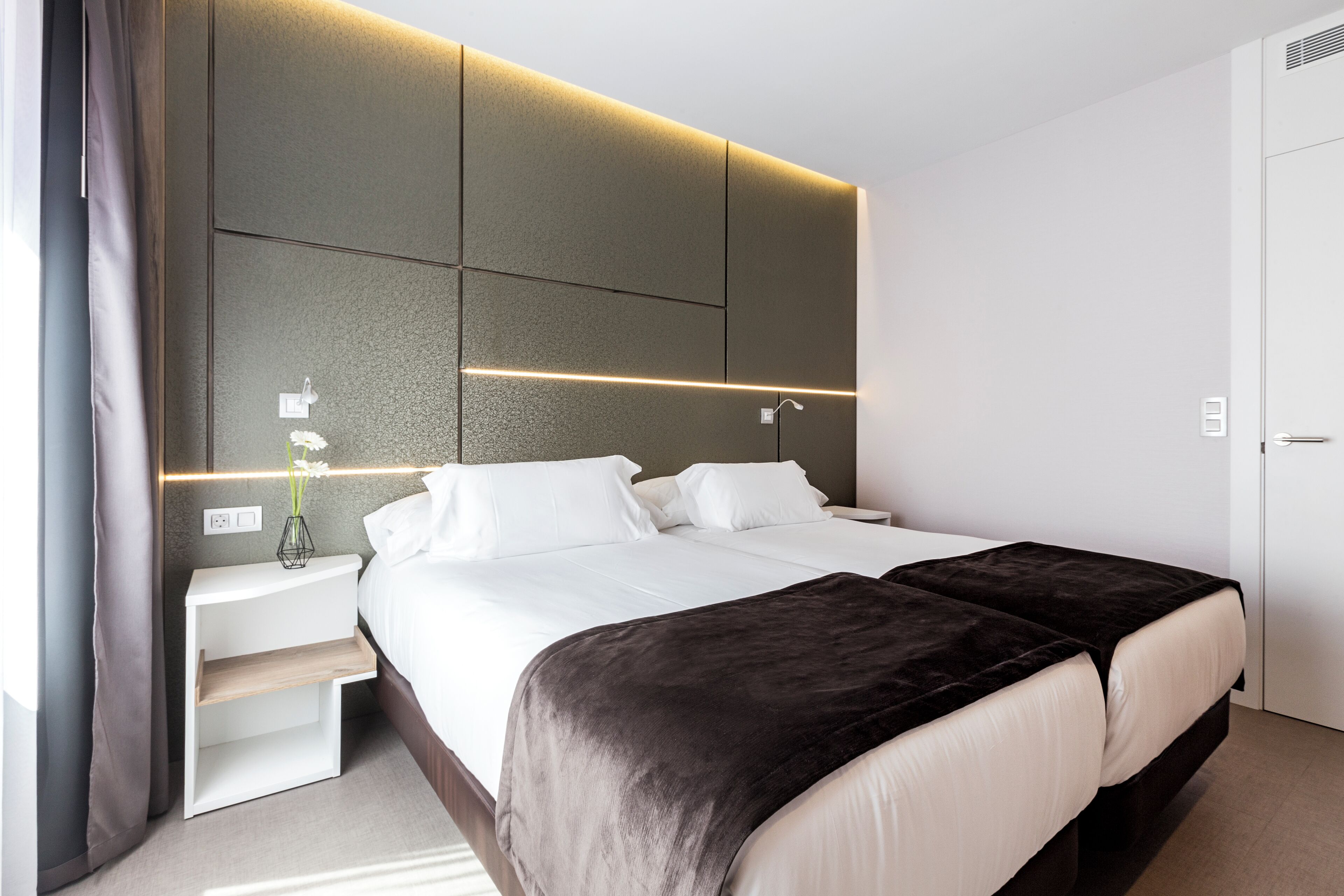 Habitació d'hotel moderna amb un llit gran, taules de nit i una làmpada de paret.