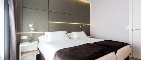A modern hotel room with a large bed, bedside tables, and a wall-mounted light fixture.