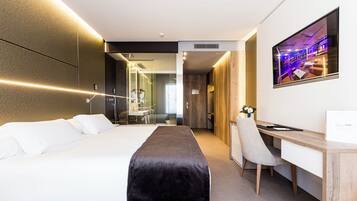 Una habitación de hotel moderna con una cama grande, un escritorio, una silla y un televisor montado en la pared.