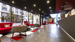 A modern lobby with red seating, large windows, and a glass partition.