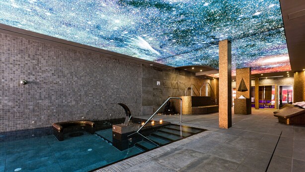 A spa area with a pool, a ceiling projection of stars, and a staircase leading to a higher level.