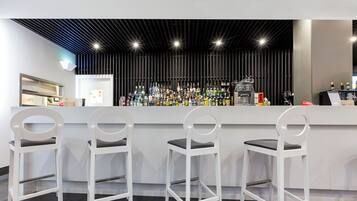 Eine Bar mit drei weißen Barhocker, einer Theke mit verschiedenen Flaschen und einem modernen Deckenstil.