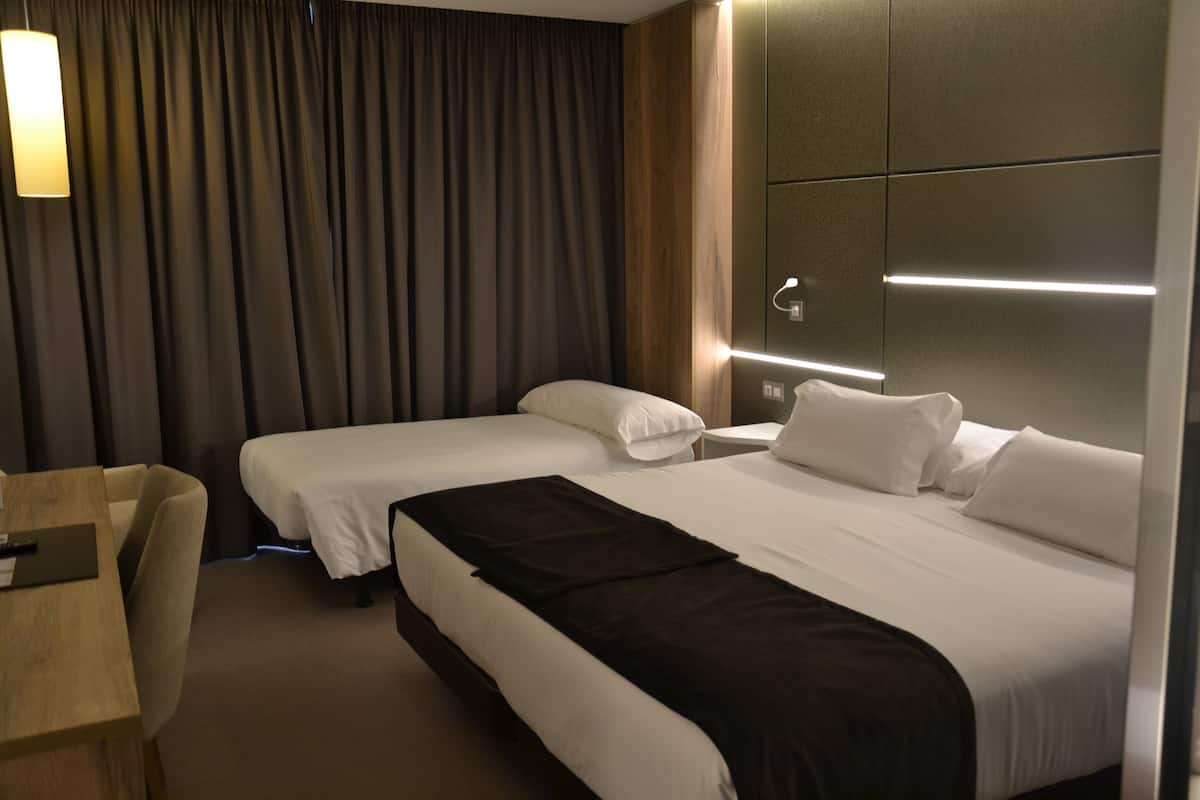 A hotel room with two beds, a desk, and a chair.