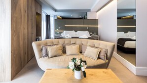A modern bedroom with a large bed, a sofa, a wooden wardrobe, and a mirror.