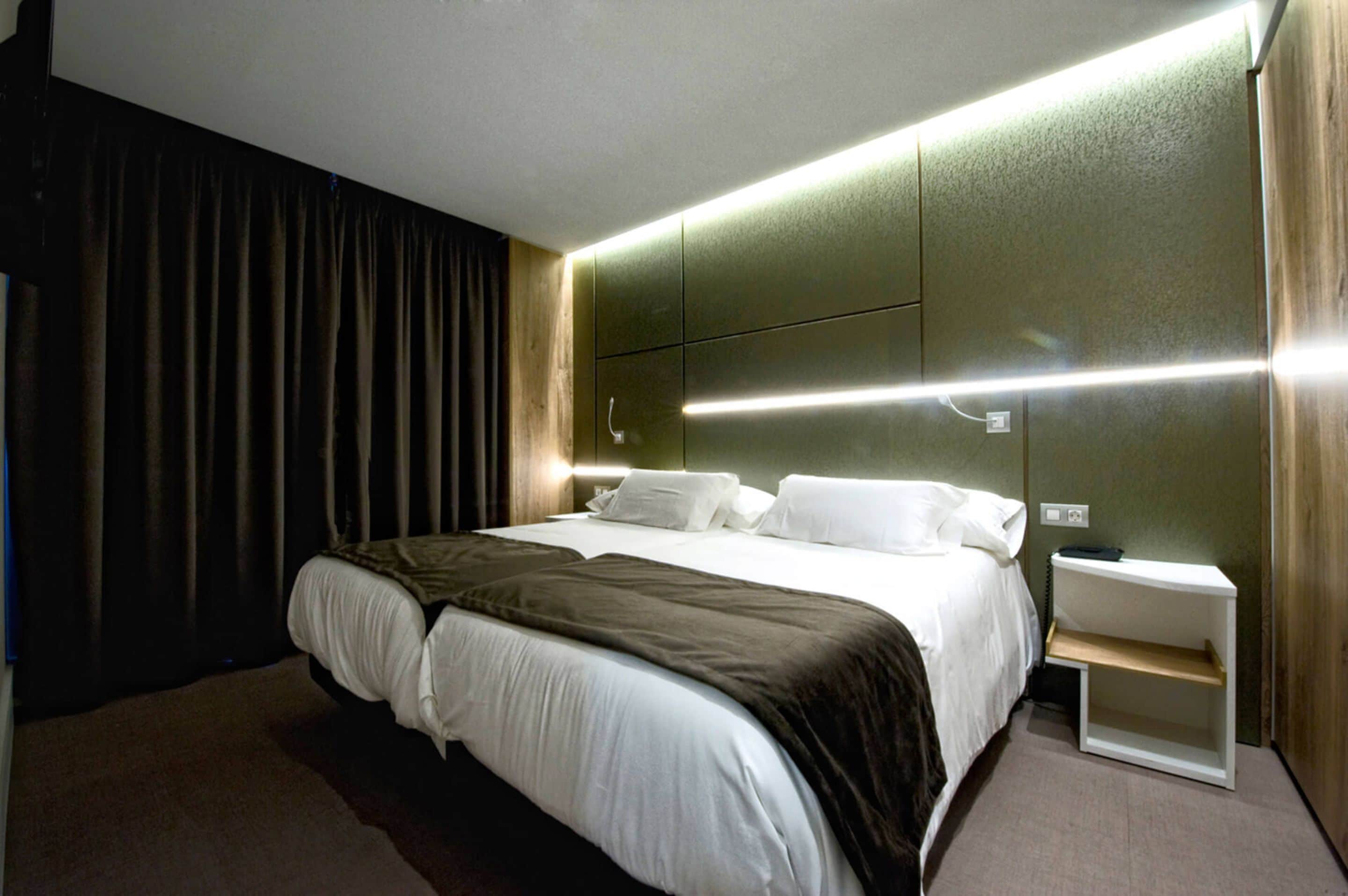 Ein modernes Hotelzimmer mit einem großen Bett, einem Nachttisch und einer integrierten Ablagefläche.