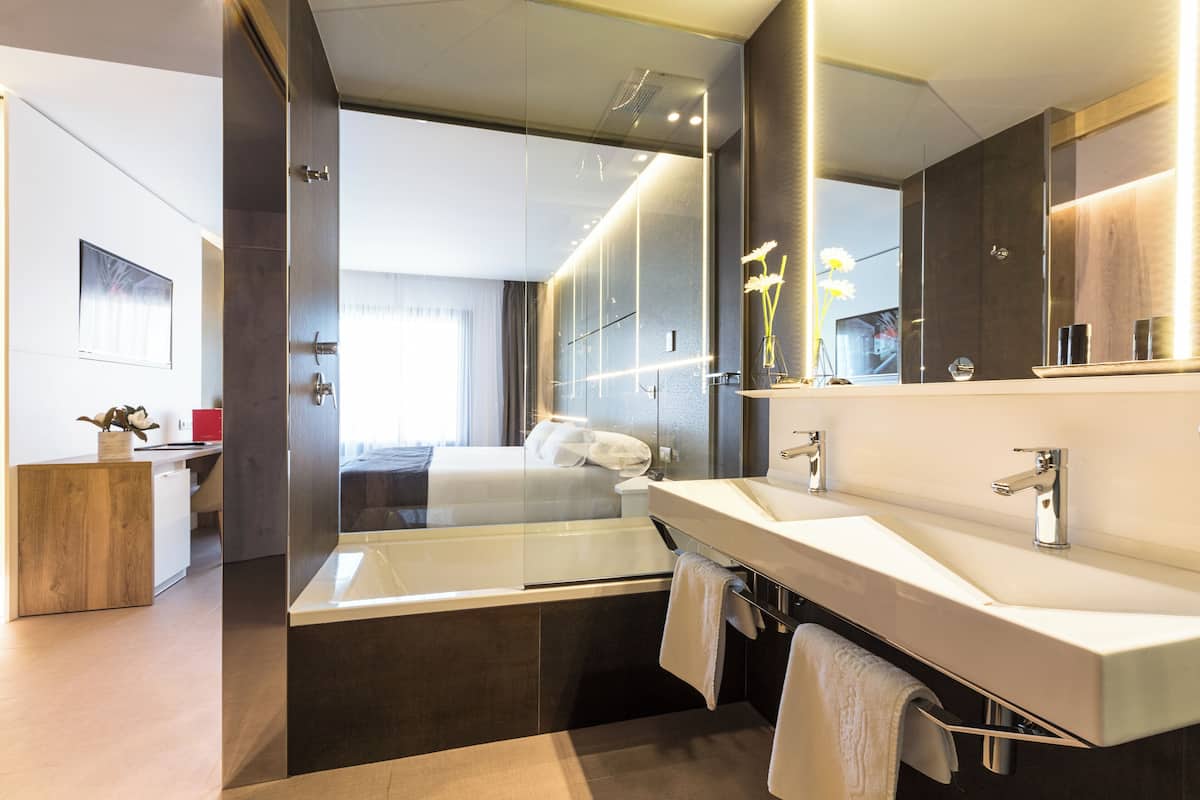 A modern bathroom with a large mirror, two sinks, and a bathtub.
