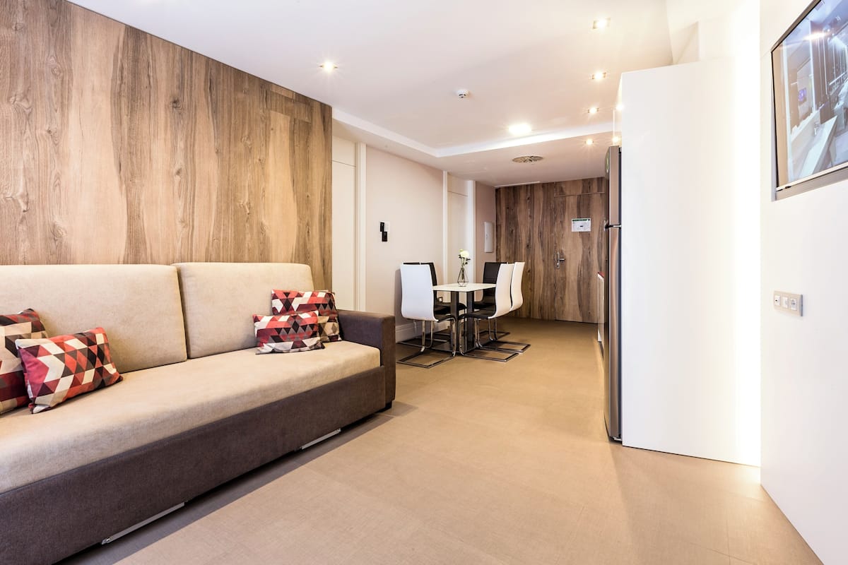 A modern living room with a sofa, a dining table with chairs, and a kitchen area in the background.
