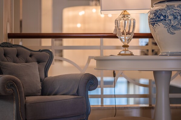 A room with a tufted armchair, a table with a decorative lamp, and a blue and white patterned vase. - Hotel Anthony (Jesolo)