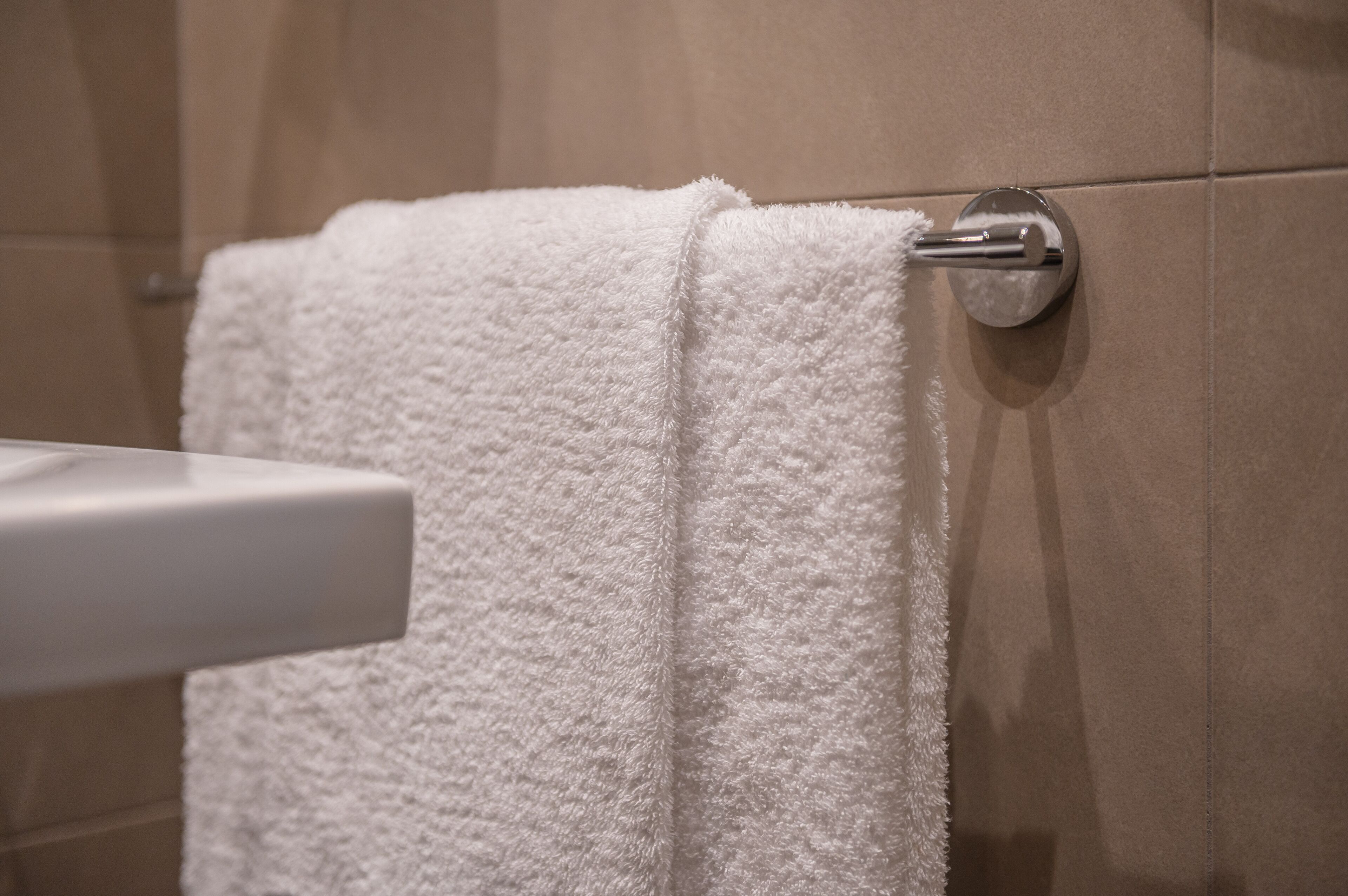 A white towel hanging on a metallic towel bar in a bathroom with beige tiles.