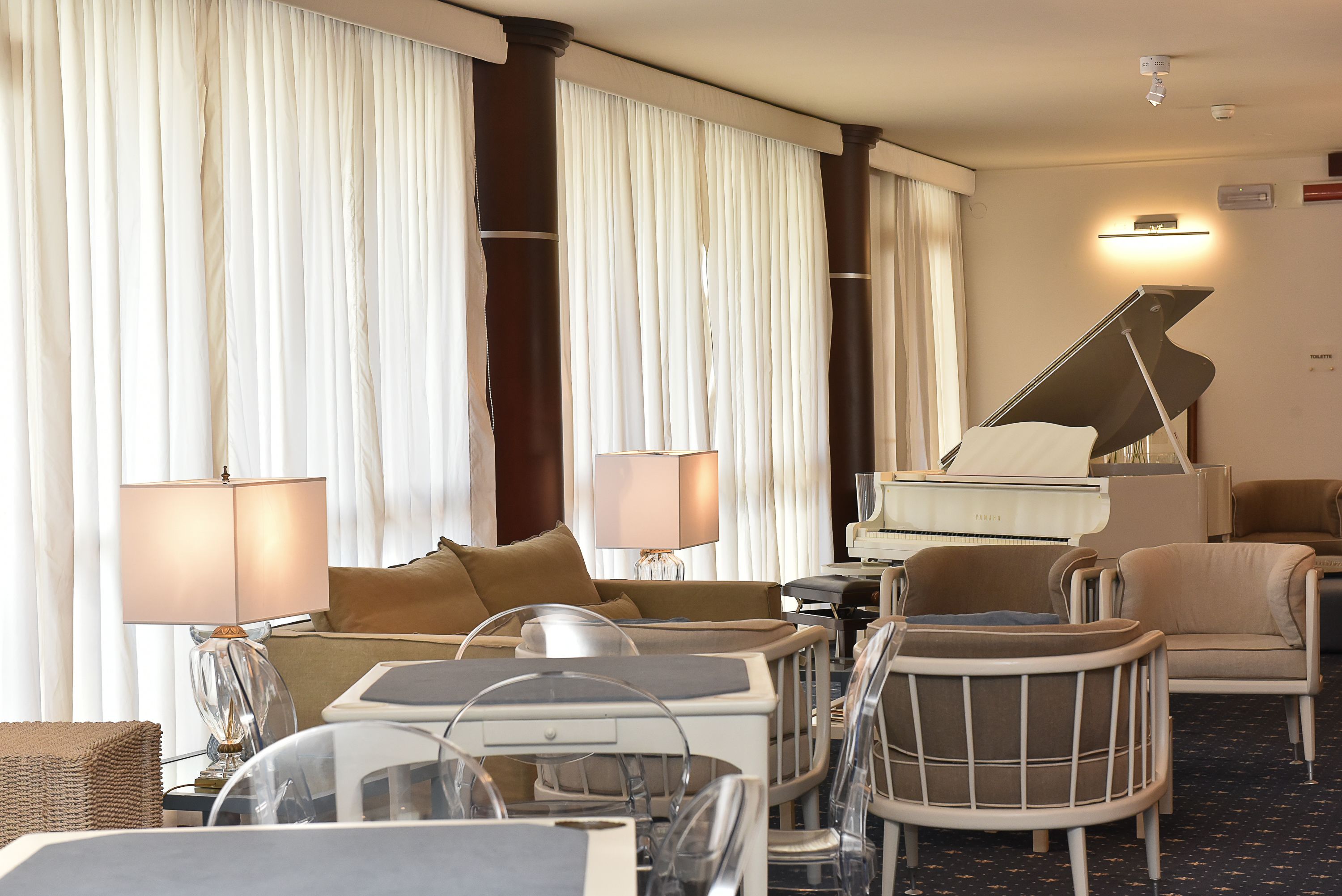 Una habitación de hotel con un piano, un sofá, una silla, una lámpara y una mesita de noche.