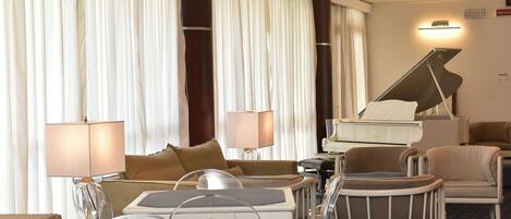 Una habitación de hotel con un piano, un sofá, una silla, una lámpara y una mesita de noche.