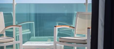 A balcony with two white chairs and a small table, overlooking a clear blue sky and a distant view.