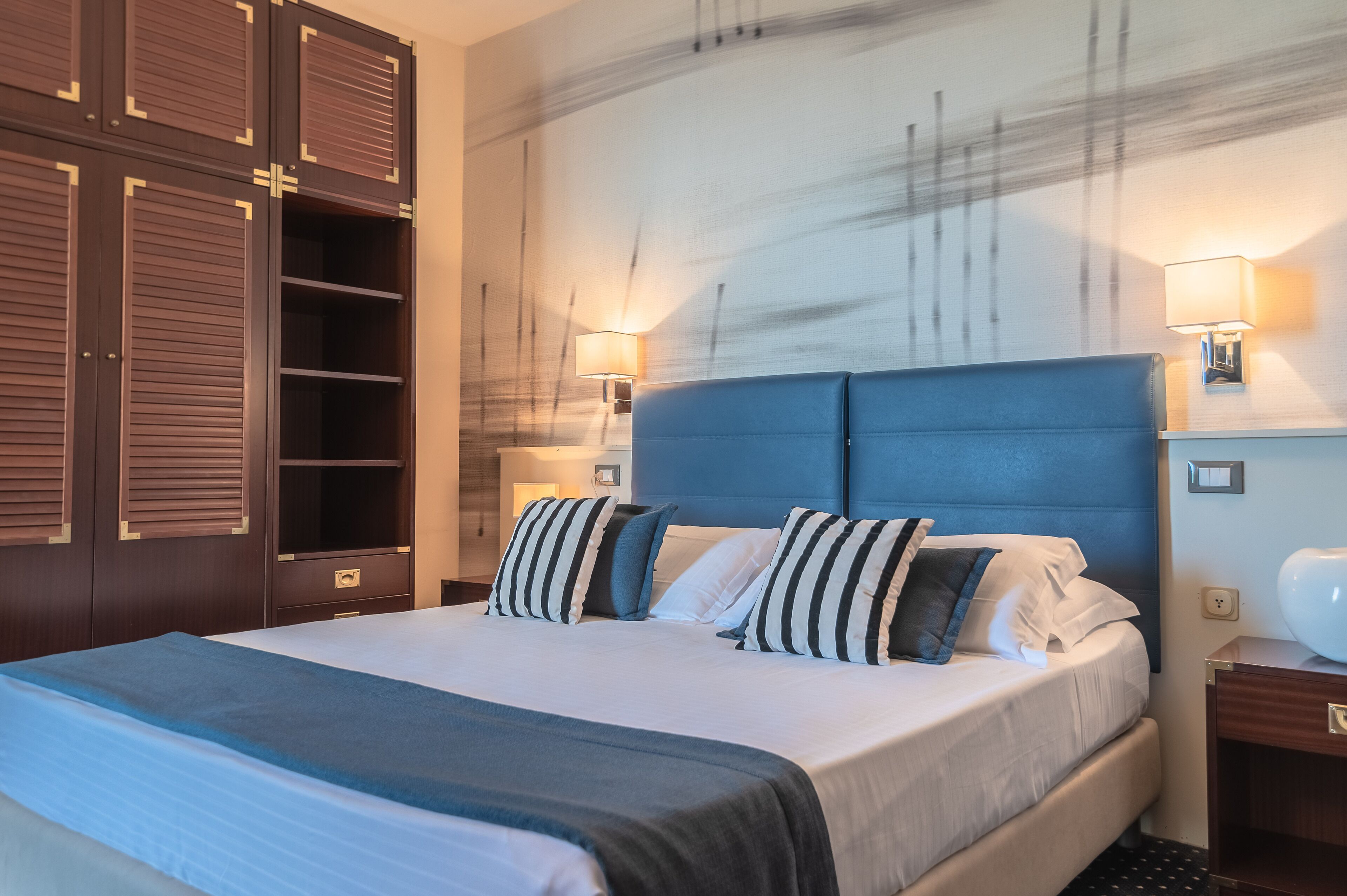 A hotel room with a large bed, a wardrobe with sliding doors, and two wall-mounted lamps.