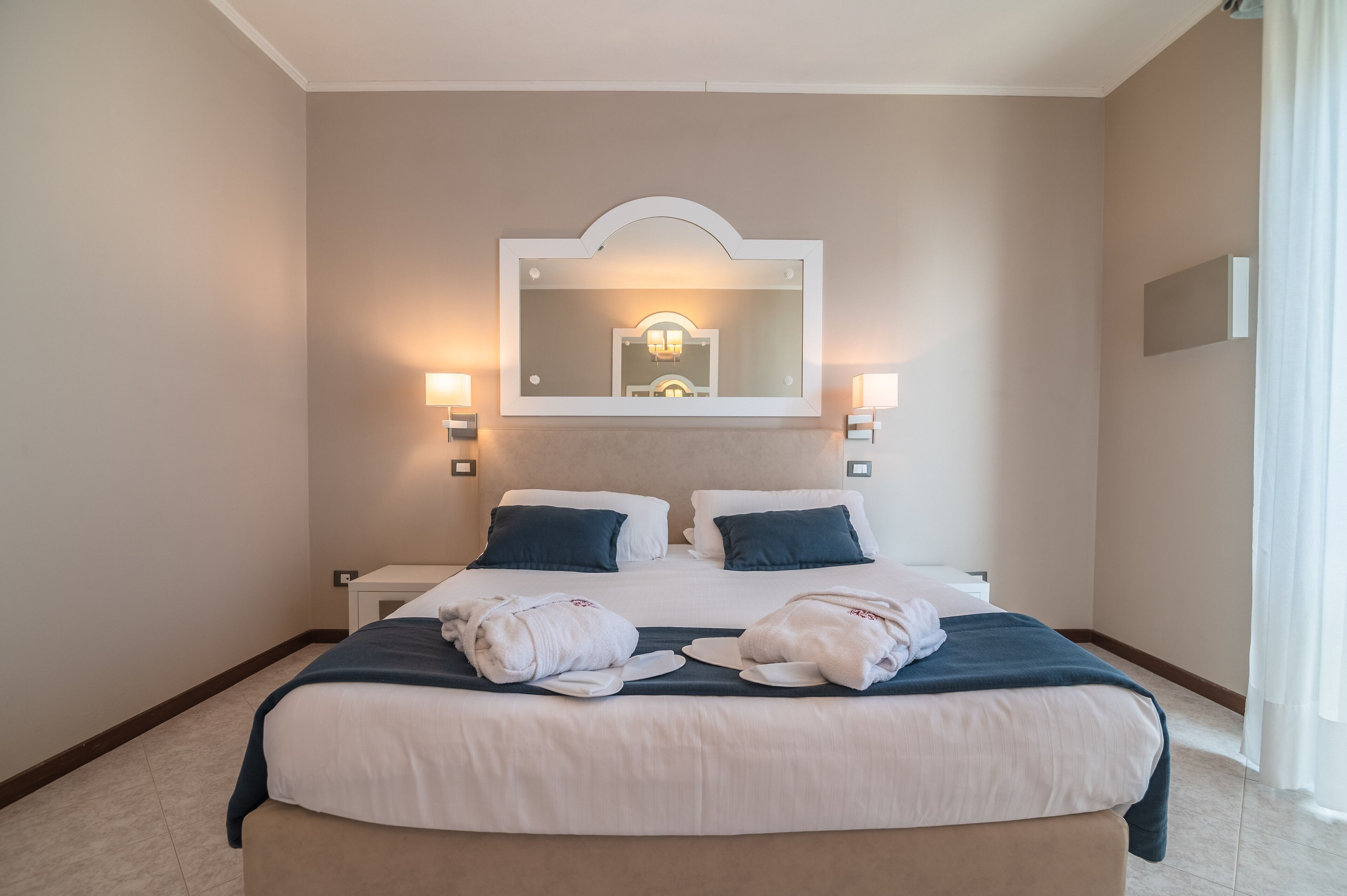 Une chambre d’hôtel avec un grand lit, deux lampes de chevet, un miroir au-dessus du lit et une vue sur l’intérieur de la pièce.