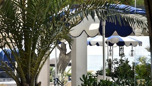 Et loungeområde ved stranden med parasoller, siddepladser og havudsigt.