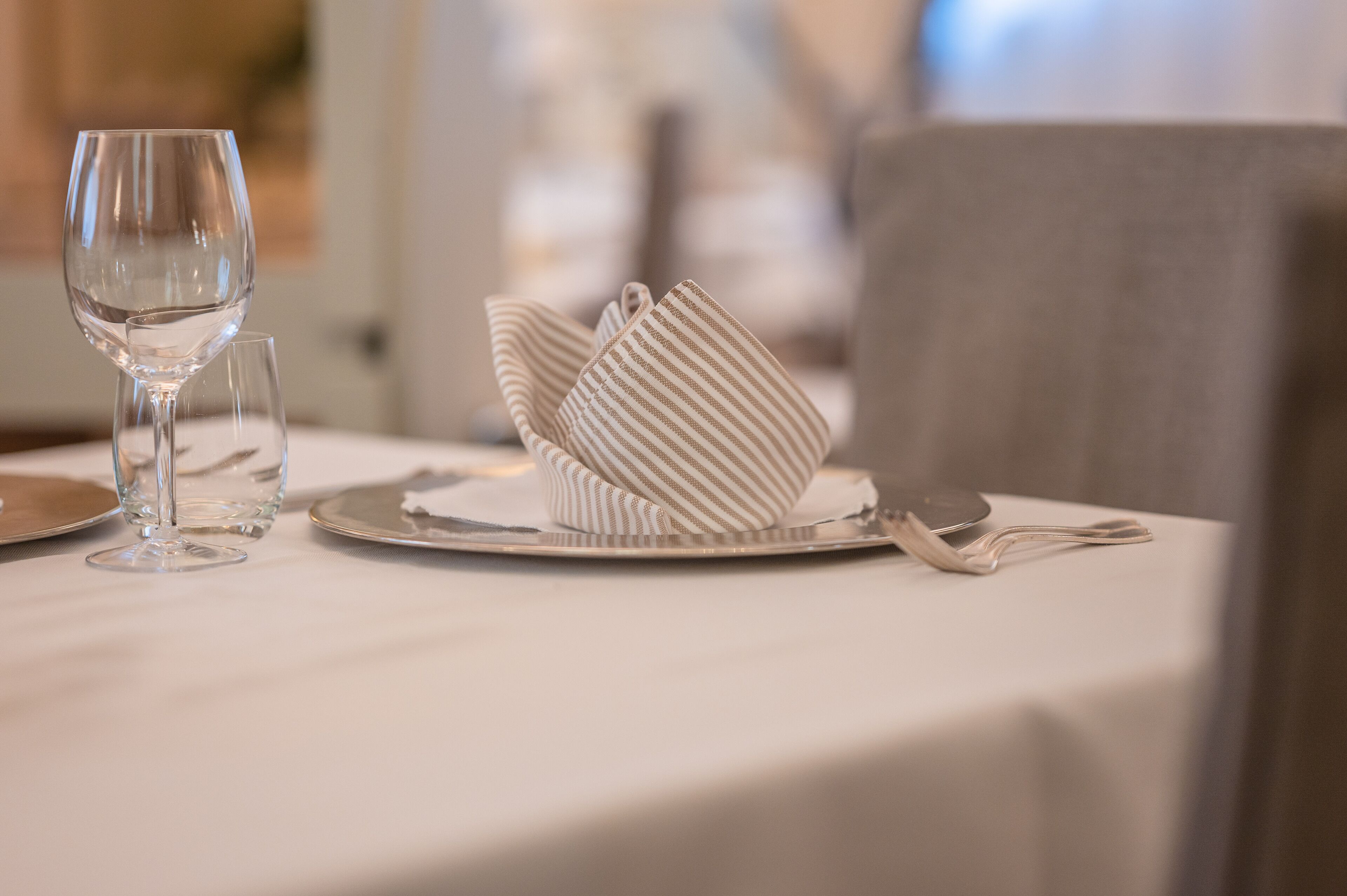 A neatly set dining table with a wine glass, a folded napkin, and a plate.