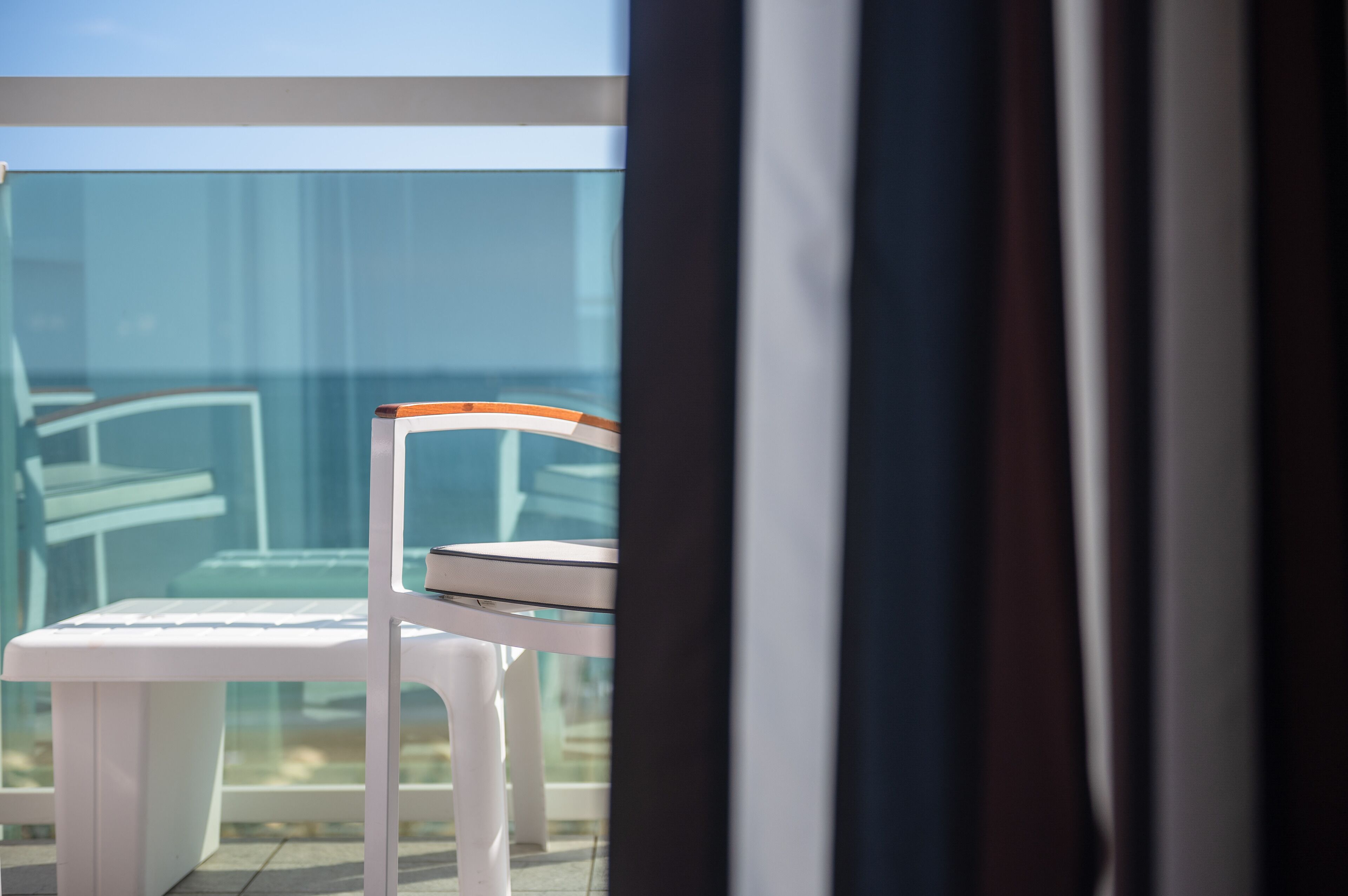 A balcony with a white chair and a glass table, offering a view of the building's interior.