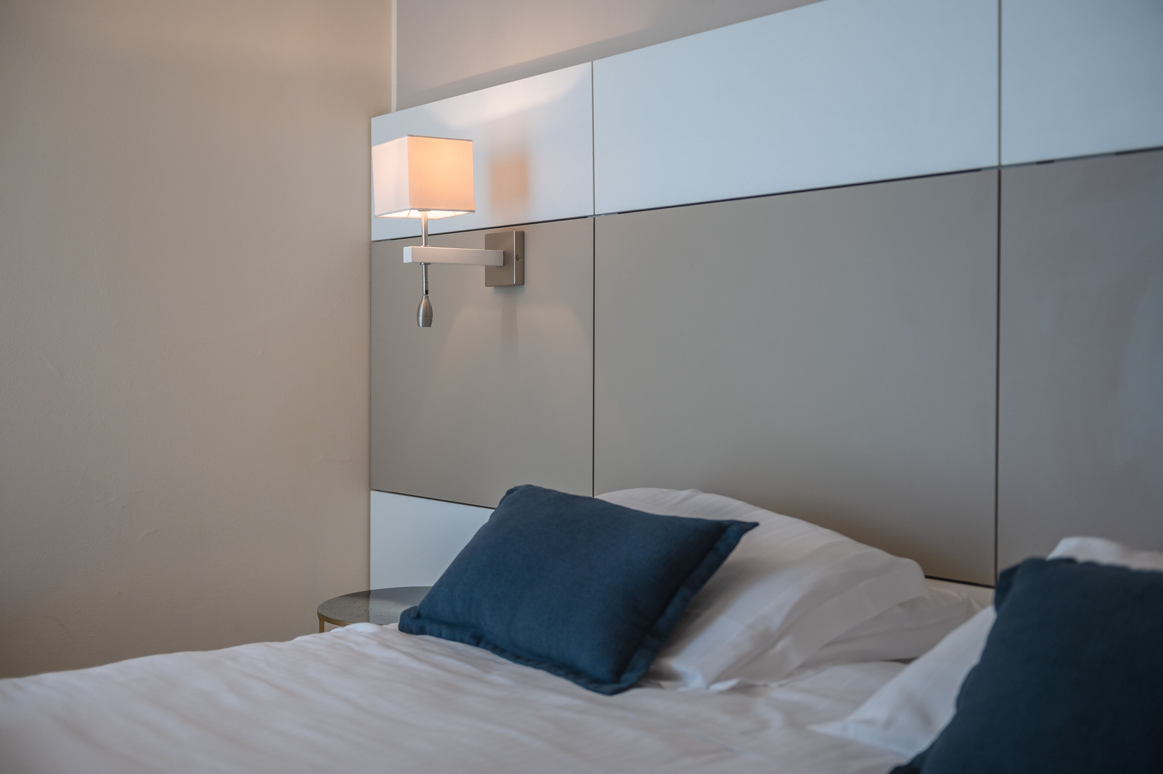 A hotel room with a bed, a nightstand, and a wall-mounted lamp.