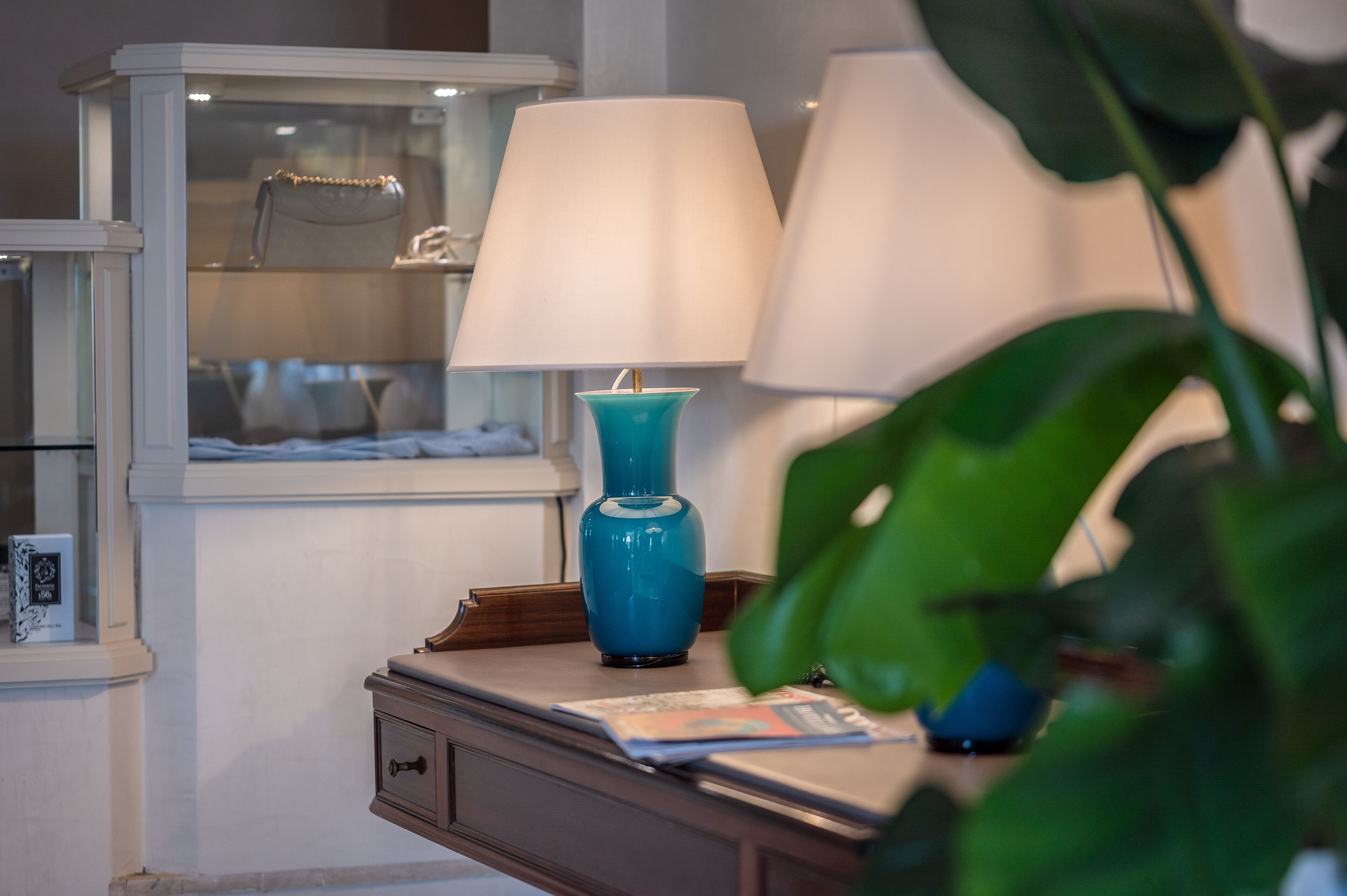 A well-lit room with a blue vase lamp, a white lamp, and a display cabinet with handbags.