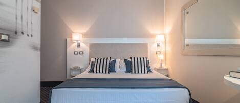 A hotel room with a large bed, two bedside lamps, a nightstand, a mirror, and a small table.