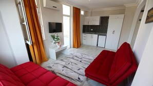 A modern living room with red sofas, a flat-screen TV, a kitchen area, and a dining table. - Hotel Paradise (Kemer)