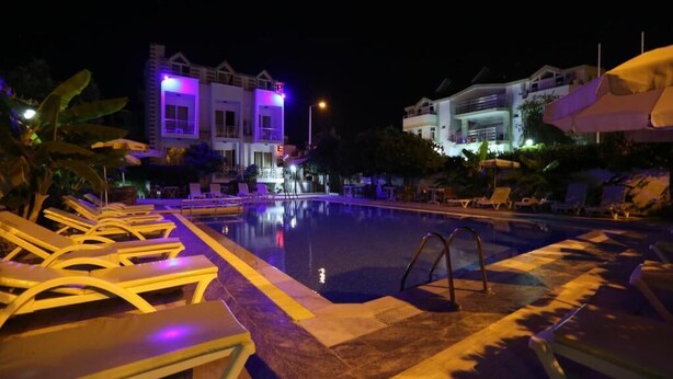 A nighttime swimming pool area with lounge chairs and a building in the background. - Hotel Paradise (Kemer)