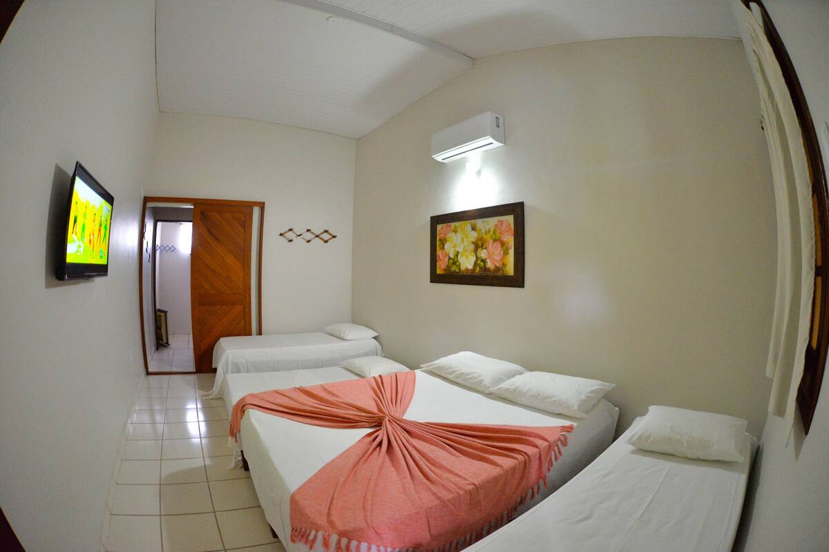 A hotel room with three beds, a television, a painting, and an air conditioning unit.