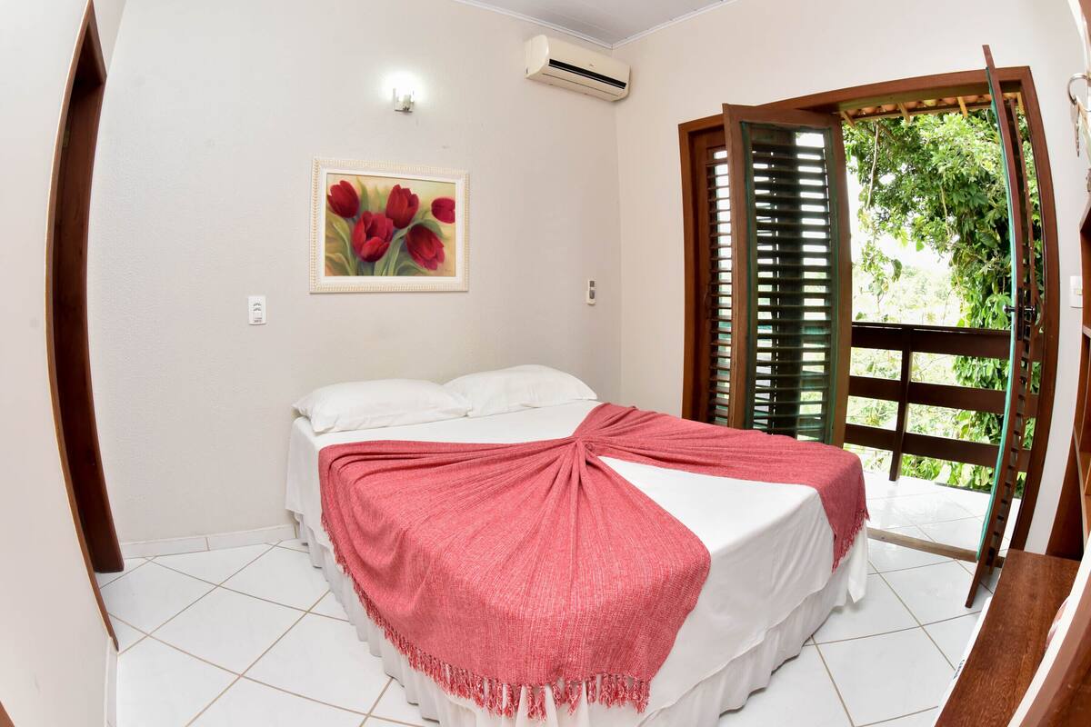 A bedroom with a bed, a painting, and a window with shutters.