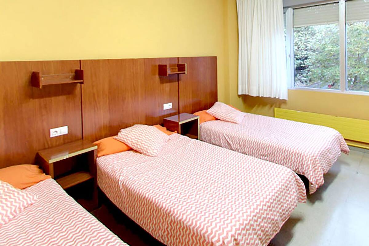 A room with three single beds, wooden headboards, and a window with curtains.