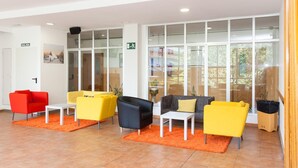 A reception area with a red chair, yellow chairs, a black chair, and a grey sofa. There is a white door labeled "SALIDA" and a green exit sign.