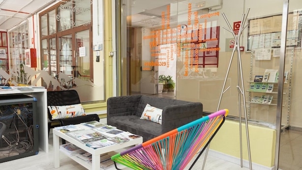 A modern office space with a grey sofa, a colorful chair, and a white table with magazines.