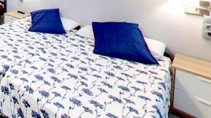 A room with a bed, two pillows, a bedside table, and a wall-mounted light.