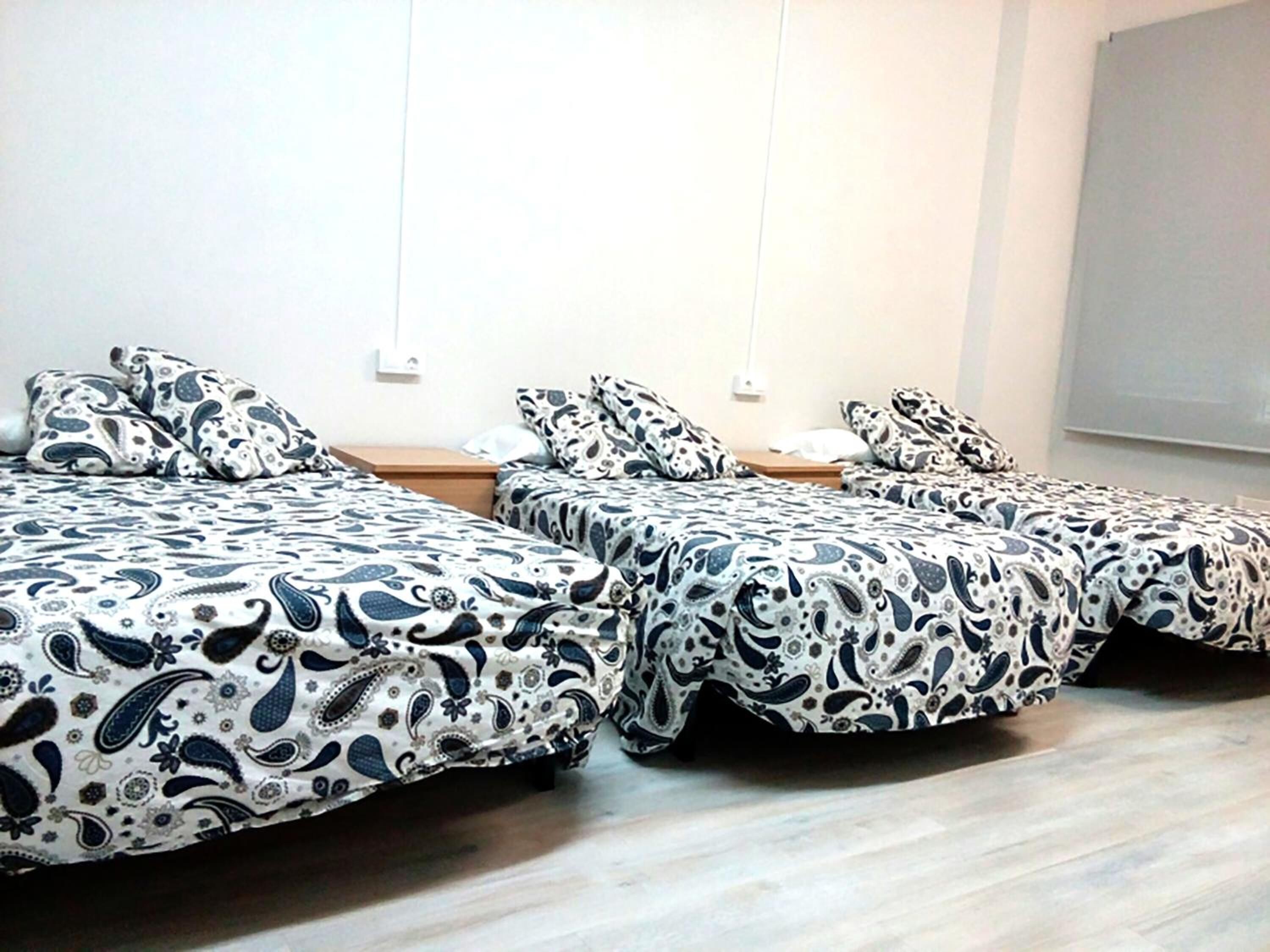 Habitación con dos camas, cada una con una colcha estampada, mesitas de noche de madera y una pared blanca con toma de corriente.