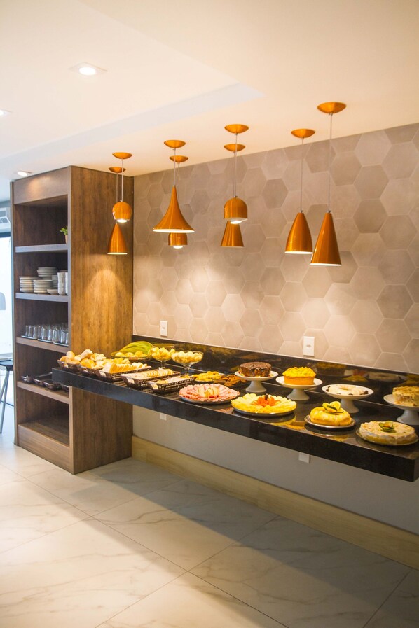 A buffet area with various food items and a modern interior design including hexagonal wall tiles and pendant lighting. - Hotel Bem Brasil (Porto Seguro)