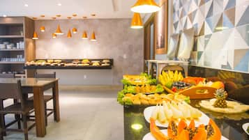 A buffet area with various fruits and dishes, a dining table with chairs, and pendant lighting.