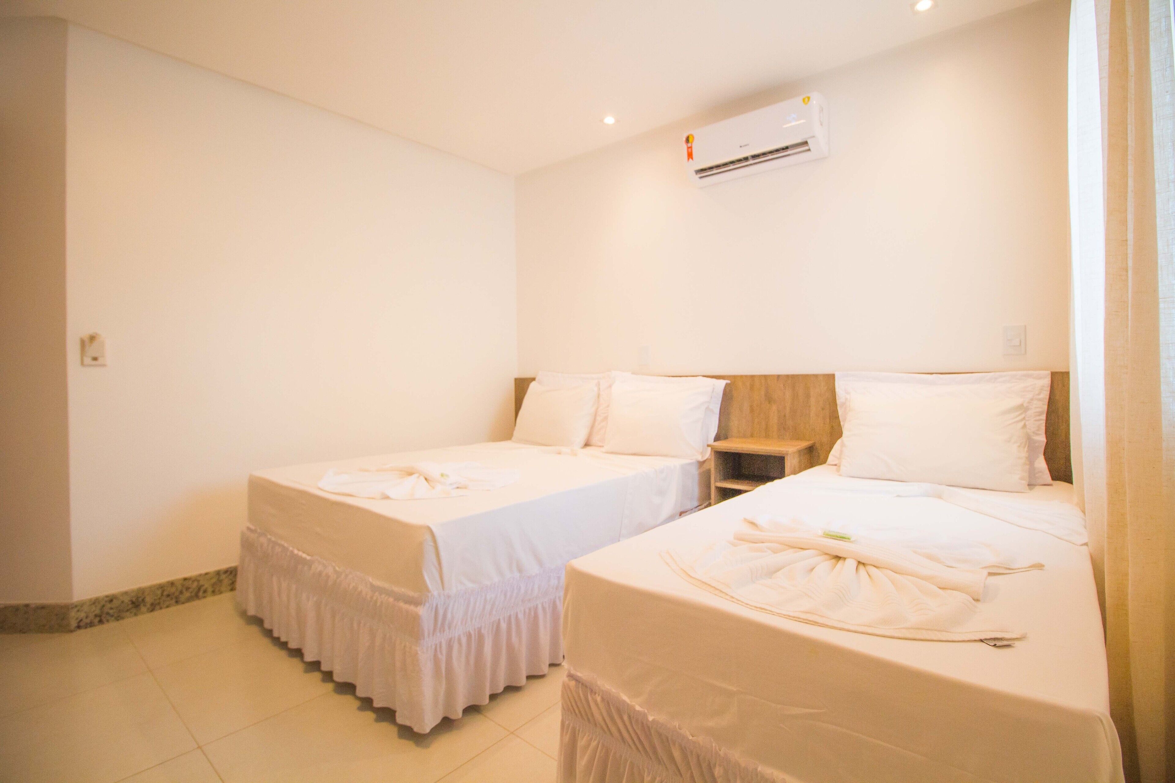 A hotel room with two single beds, a wooden nightstand, a wall-mounted air conditioner, and a tiled floor.