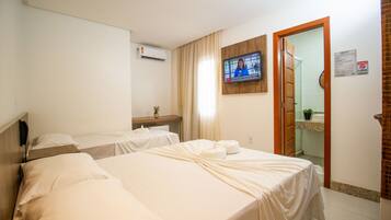 A hotel room with two beds, a TV mounted on the wall, an air conditioner, and a bathroom visible through an open door.