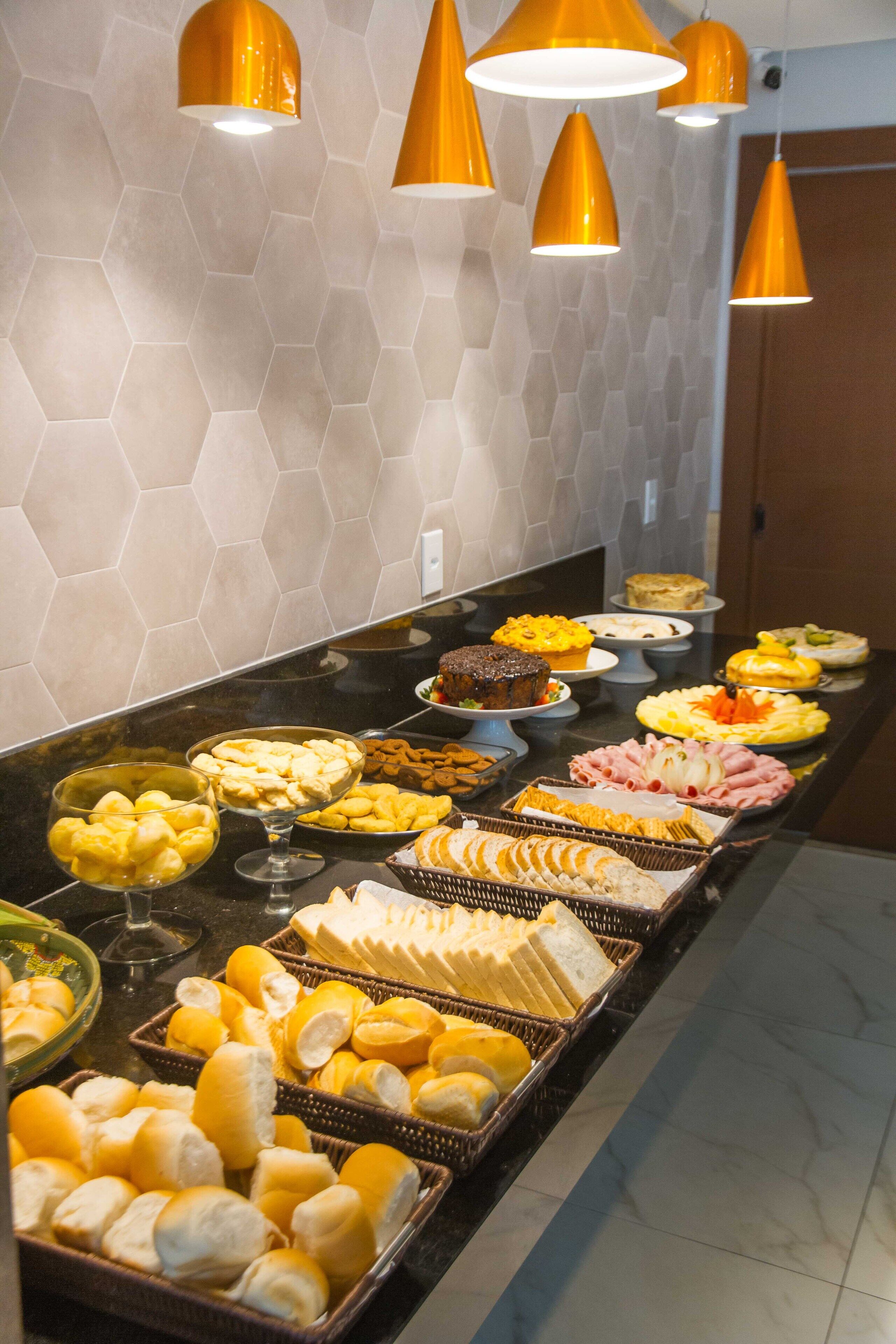Buffet com diversos alimentos e parede revestida com azulejos hexagonais.