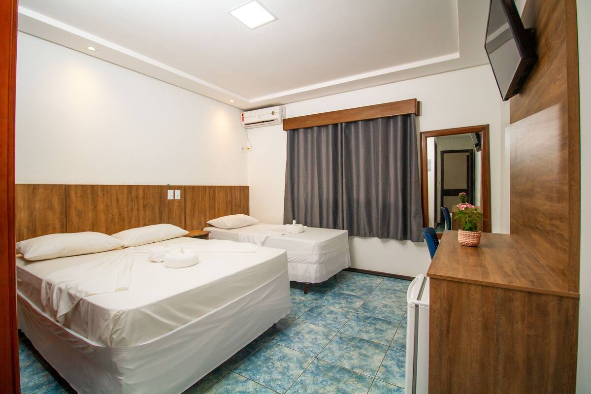 A hotel room with two beds, a wooden headboard, a TV mounted on the wall, and a desk with a plant.