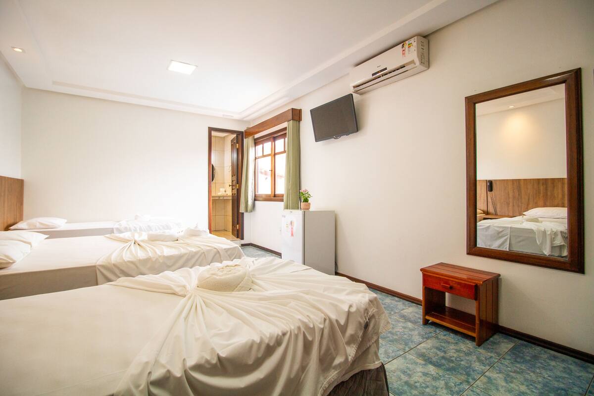 A hotel room with two beds, a small bedside table, a mirror, a TV, and an air conditioning unit.