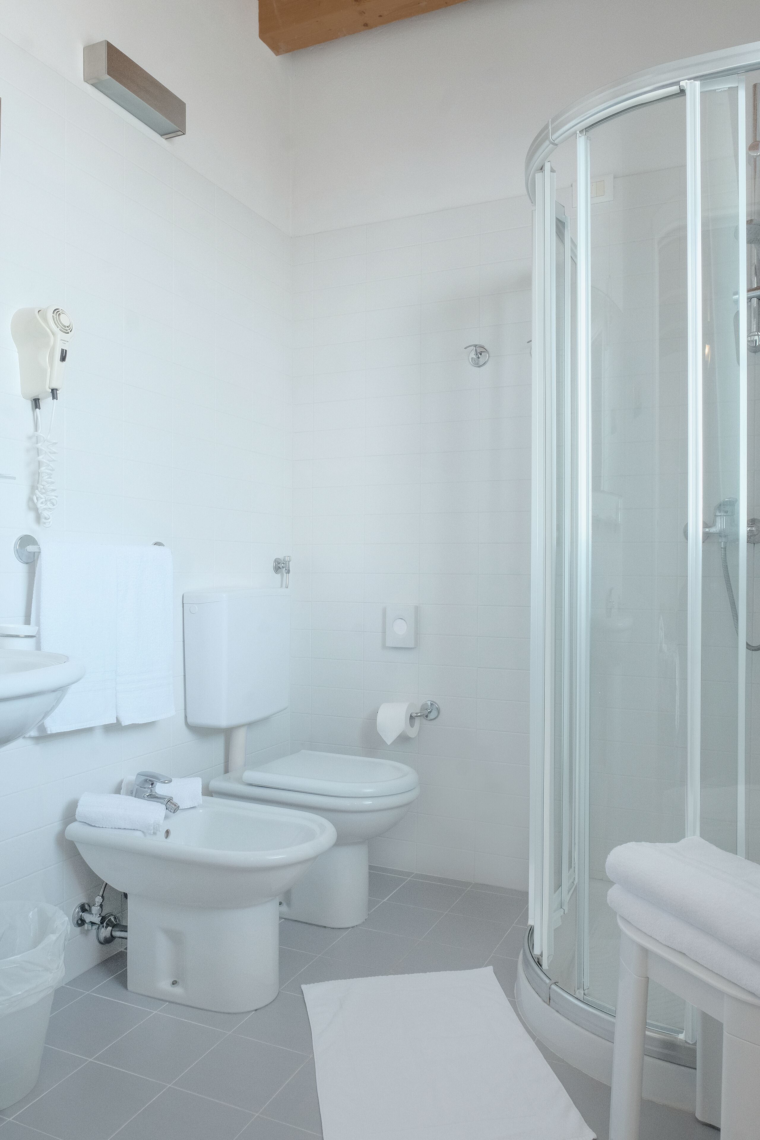 A modern bathroom with a glass-enclosed shower, two toilets, a bidet, and a sink.