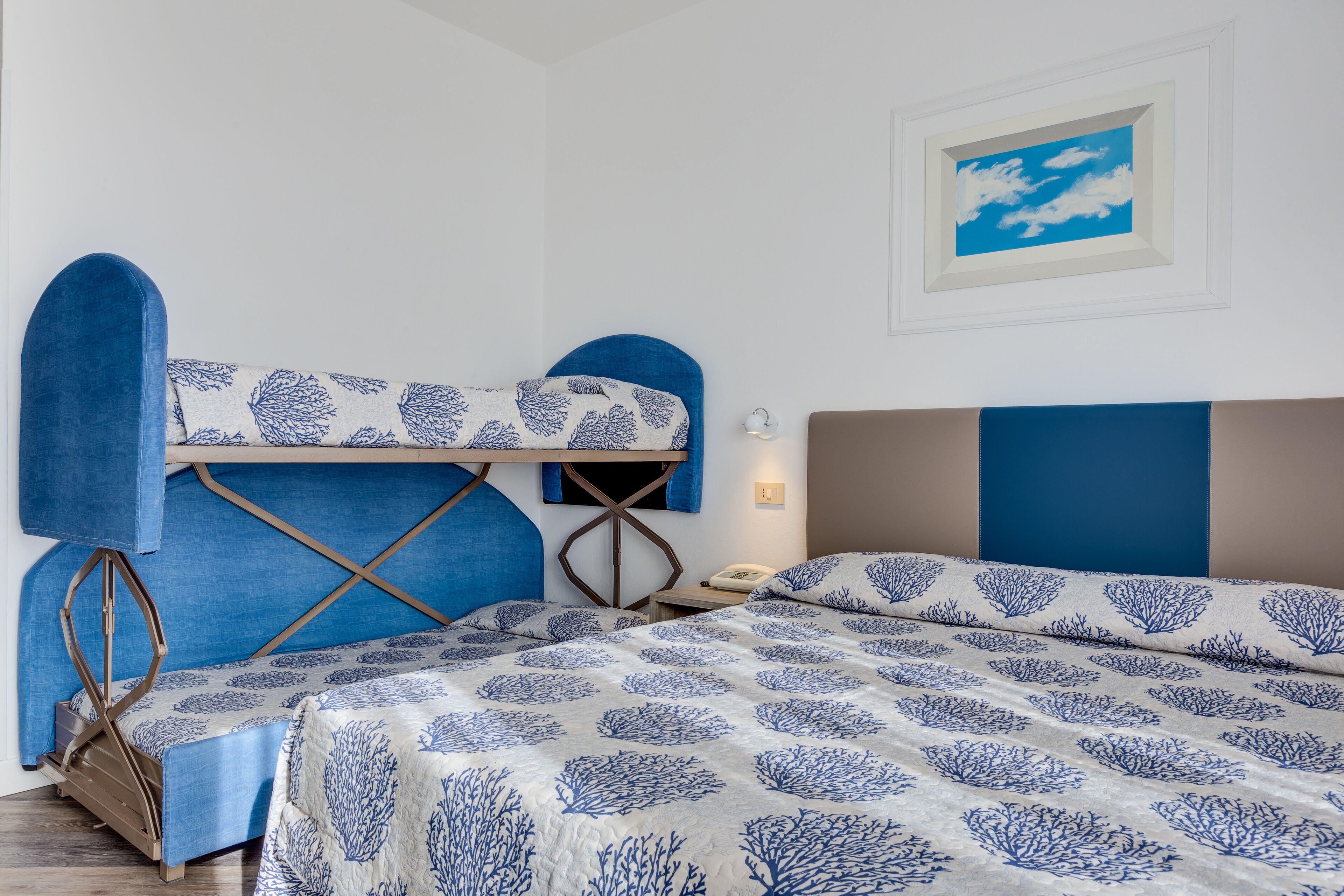Un lit superposé avec une tête de lit bleue et un lit inférieur recouvert d’une couvre-lit à motifs.