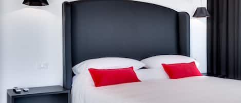 A modern bedroom with a large bed, two red pillows, a nightstand, and two pendant lights.