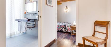 A bathroom with a shower, a sink, and a mirror. There is a wooden chair in the room.
