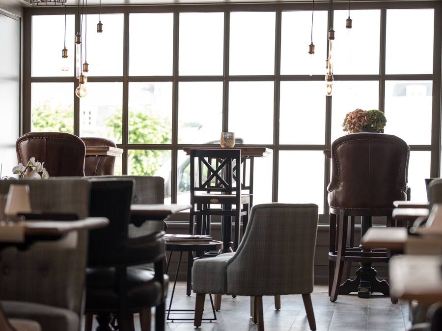 A cozy cafe with leather chairs, a wooden table, and hanging light fixtures.