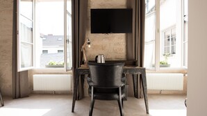 A room with a desk, a chair, a radiator, and a TV mounted on the wall. - Hôtel Le Chantilly (Chantilly)